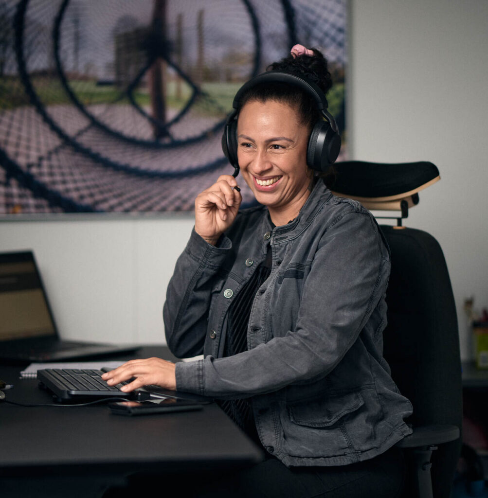 Smilende medarbejder hos DALPIN sidder ved computer med headset klar til at besvare spørgsmål.